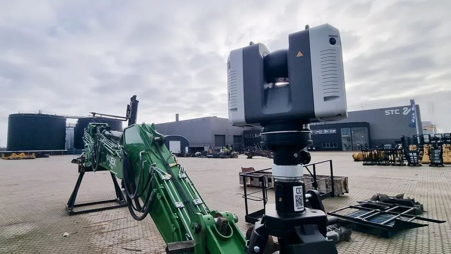 Artec Ray II on a tripod beside the hydraulic arm of an excavator in a machinery yard
