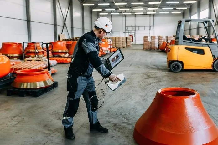 Engineer 3D scanning a cone crusher mantle in a spare parts warehouse